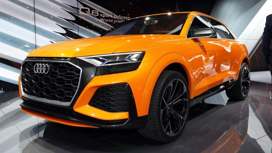 На фото новый шикарный автомобиль Audi Q8 ярко-оранжевого цвета в автомобильном салоне