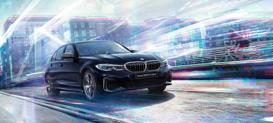 На фото автомобіль BMW 3 серії G20 чорного кольору мчить міською дорогою