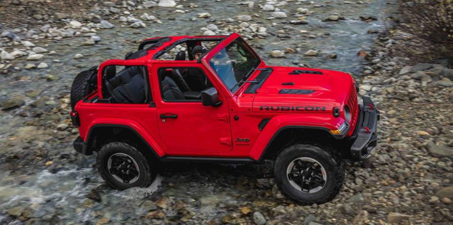 На фотографии красный 2-х дверный Jeep Wrangler 2018-2019 с открытой крышой переезжает через горную речку