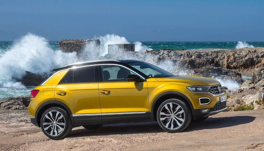 На фото автомобиль Volkswagen T-Roc двухцветной окраски кузова горчичного и черного цвета стоит у побережья с брызгами волн