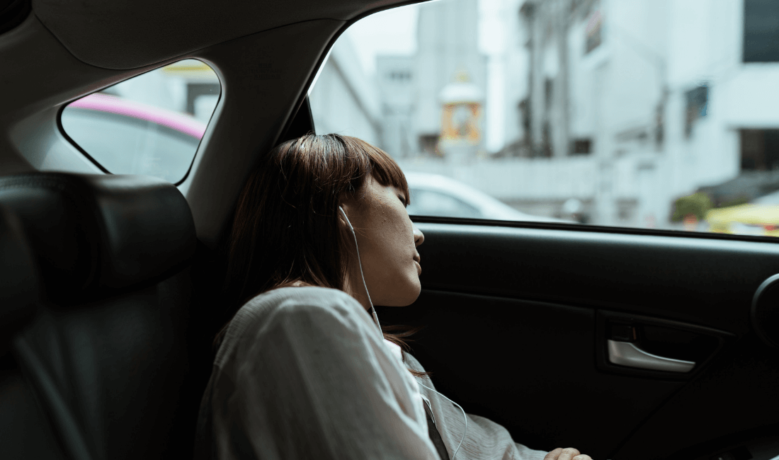 На фото женщина, на заднем сиденье авто, слушает музыку в наушниках и закрыла глаза, чтобы ее не укачивало