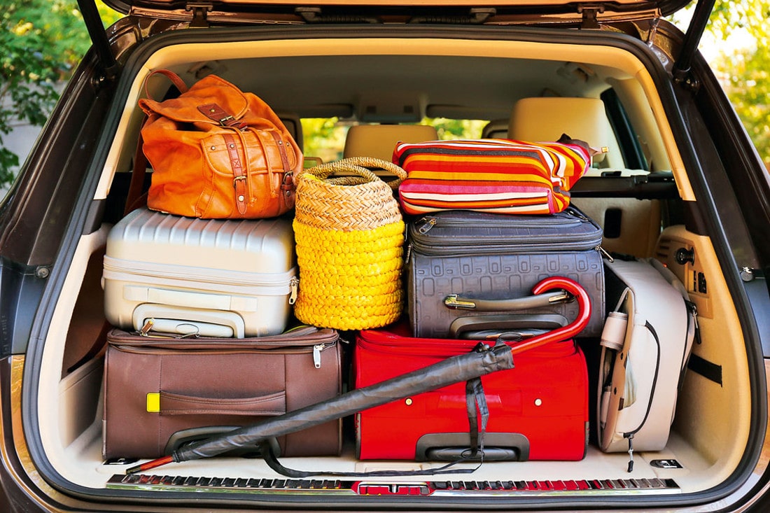 На фото открытый багажник автомобиля полностью заставленный чемоданами, сумками и вещами ярких цветов
