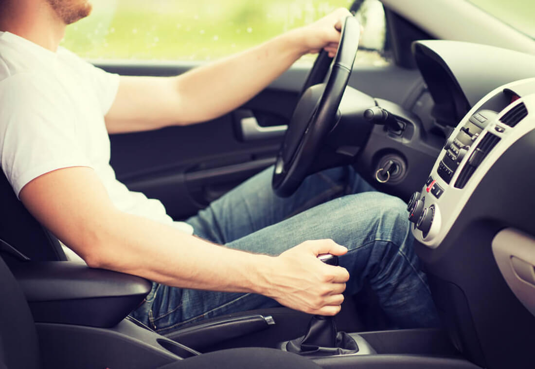 На фото водитель правильно сидящий за рулем автомобиля. Его левая рука на руле, правая - на коробке передач
